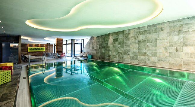 Beleuchtetes Hallenbad mit grün schimmerndem Wasser im Hotel Dorfstadl