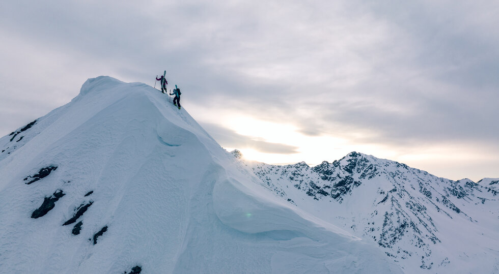 Skitourengeher auf einem verschneiten Gipfelgrat mit Bergpanorama im Paznaun