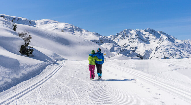 Paar beim Winterwandern auf einem geräumten Weg mit Bergkulisse im Paznaun