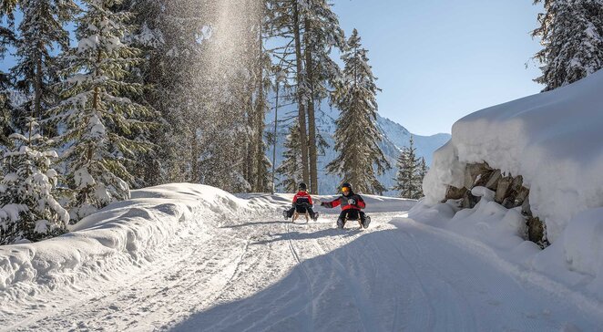 Zwei Rodler auf der Rodelbahn Kappl im tief verschneiten Winterwald