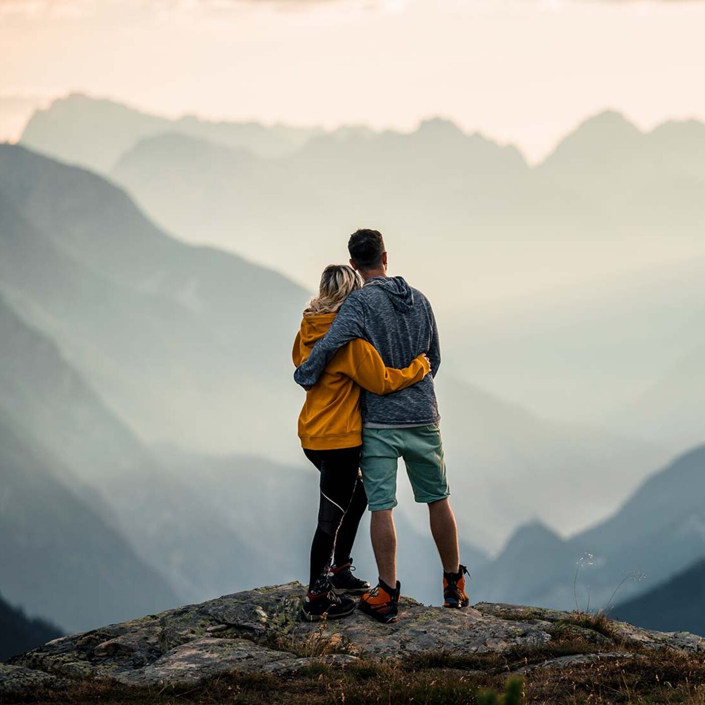 Paar steht umarmt auf einem Felsen am Mittagskopf und blickt über die Berge bei Kappl