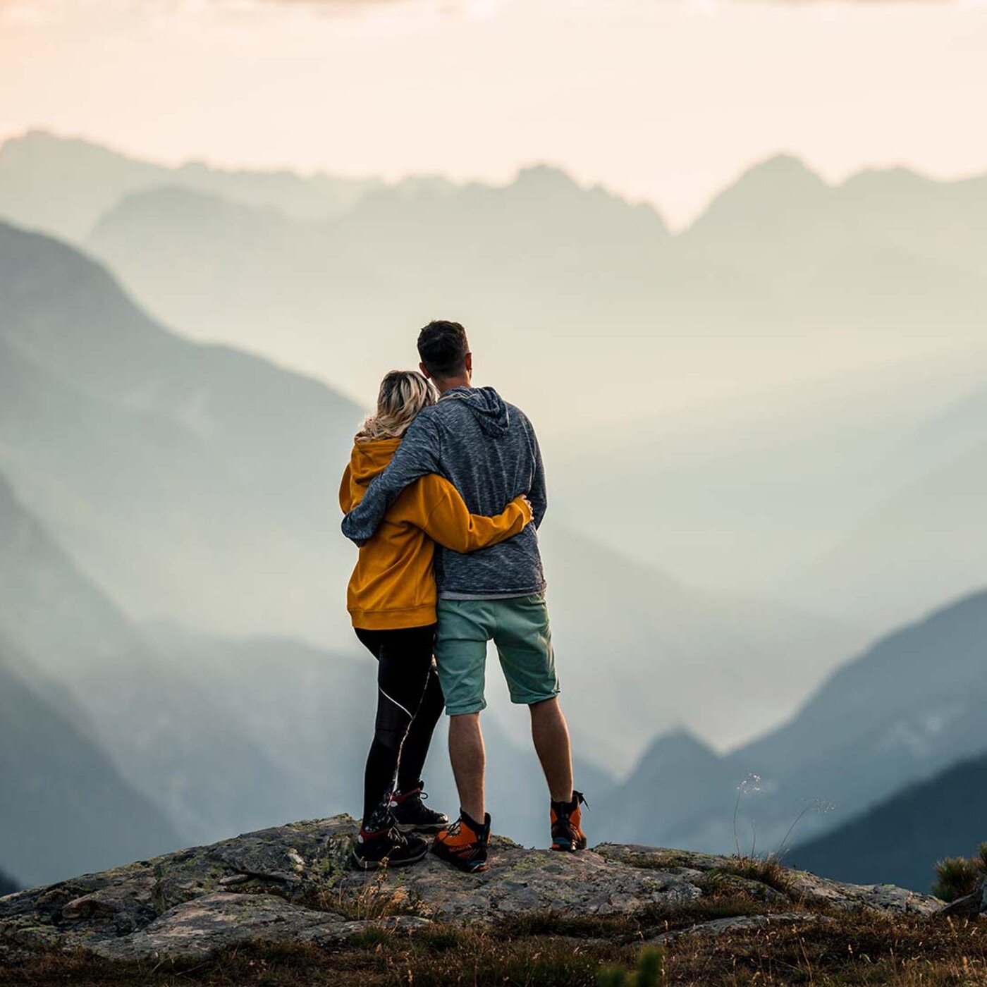 Paar steht umarmt auf einem Felsen am Mittagskopf und blickt über die Berge bei Kappl
