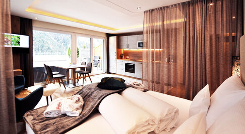 Doppelbett mit Kuscheldecke und Blick in den Wohnbereich eines Appartements im Hotel Dorfstadl