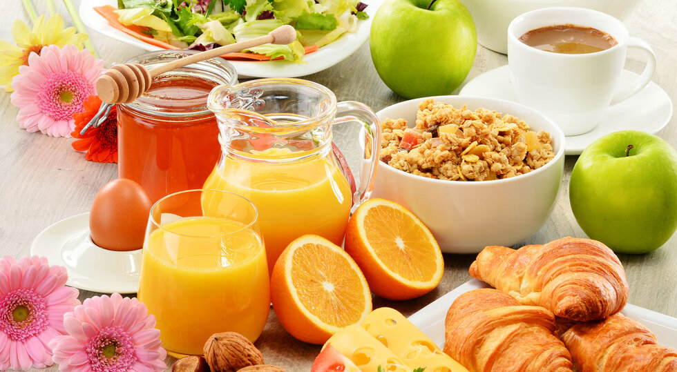 Buntes Frühstück mit Orangensaft, Müsli, Croissants, Obst und Kaffee